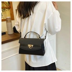 Detail view of black textured leather handbag with gold metal lock and chain accessory