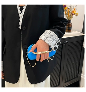 Detail of vibrant blue clutch bag featuring a gold horseshoe handle and chain strap