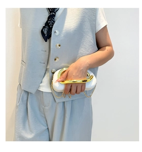 Detail of white leather clutch with oversized gold sculptural handle and chain strap