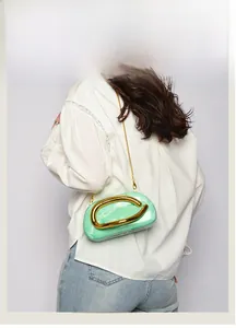 Green marble acrylic clutch bag with C-shaped gold handle worn over white shirt