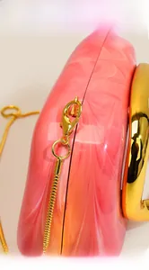 Detail of pink marble acrylic clutch featuring polished gold chain and lobster clasp