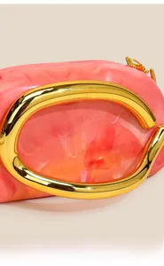 Detail of pink marble acrylic clutch featuring polished gold C-shaped metal handles