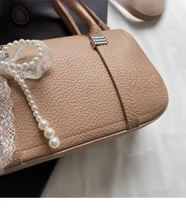 Dettaglio della borsa in pelle marrone chiaro con ciondolo di perle e chiusura d'argento