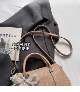 Dettaglio borsa beige in pelle martellata con fiocco di perle e tracolla regolabile