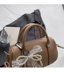 Dettaglio borsa Boston con manico arrotondato e ciondolo a fiocco in pizzo e perle