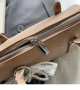 Dettaglio della cerniera argentata su borsa in pelle beige con ciondolo di perle