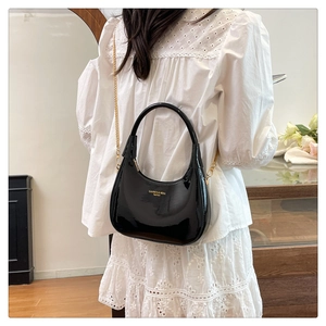 Detail of elegant black patent leather crescent bag with gold chain and brand logo