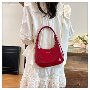 Detail of red patent leather hobo bag featuring gold lettering and a thin metal chain strap