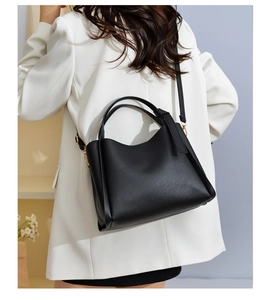 Detail of black lychee grain leather bucket bag with pale gold hardware and crossbody strap