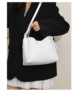 Detailed shot of white litchi grain leather bucket bag worn with a black blazer