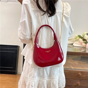 Chic bright red patent leather hobo bag with gold chain strap shown on a model
