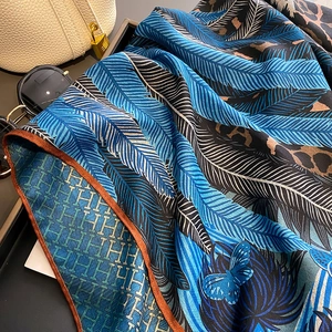 Silk scarf featuring leopard and blue feather patterns draped on a white leather bag