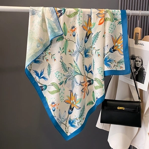 Elegant floral silk scarf with orange and blue prints draped next to a luxury handbag