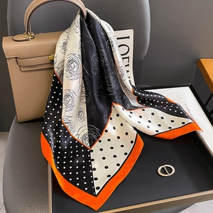 Foulard en soie avec motif rose à pois et bordure orange drapé sur un sac de créateur