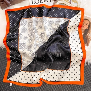 Détail d'un foulard en soie avec motifs de roses, pois et bordure orange contrastée