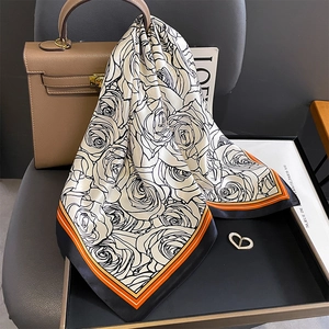 Silk square scarf with rose floral print and orange border draped on a designer handbag