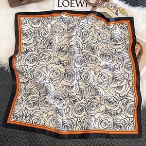 Detail view of square silk scarf with floral rose pattern on white plush background