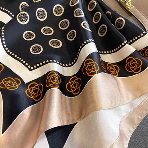 Silk camellia pattern square scarf draped over a luxury leather handbag