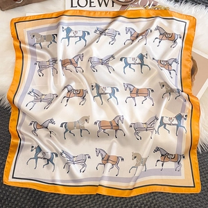 Detail view of square silk scarf with horse print and vibrant orange border on plush background
