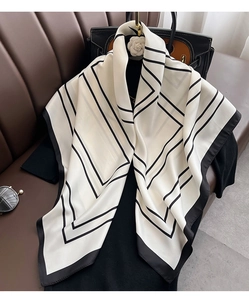 Détail d'un foulard en soie à bordures géométriques drapé sur une tenue noire élégante