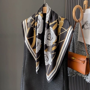 Detailed close-up of a silk-feel scarf with white camellia flowers and golden chain prints