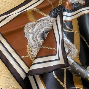 Detail of silk-like scarf with vintage floral camellia patterns and golden chain design