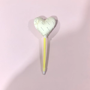 Makro-Detail des creme-weißen Herzschmucks mit Strass und Schleife auf gelbem Stift