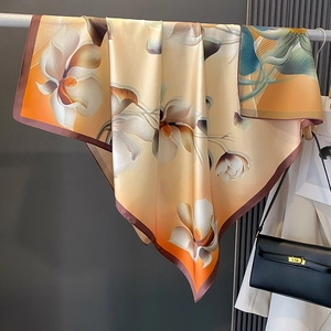Écharpe élégante en soie avec imprimés magnolia et dégradés orange sur un cintre argenté
