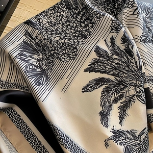 Beige silk scarf with black palm leaf prints and striped borders in a soft drape