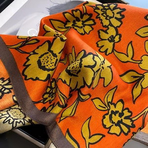 Close-up of bright orange floral scarf showing twill texture and brown herringbone hem