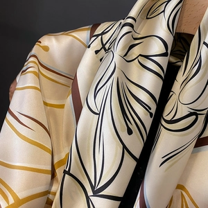 Elegant cream silk scarf with floral print and satin luster on a wooden hanger