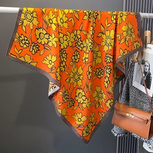 Macro view of orange square silk scarf featuring yellow floral prints and dark brown borders