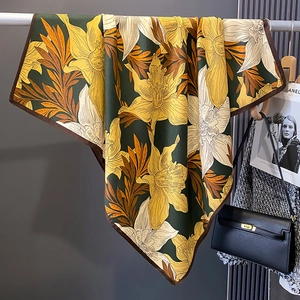 Detailed drape of green floral square silk scarf with large yellow lilies and brown hem