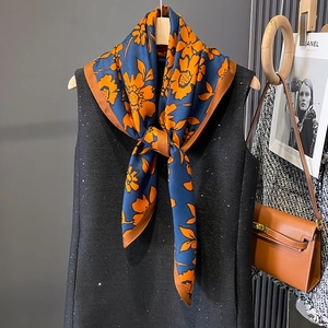 Floral printed large scarf in navy blue and orange, styled on a wooden hanger with a vest