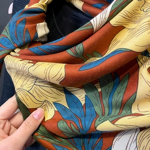 Close-up of floral print scarf in yellow and orange on a dark textured coat