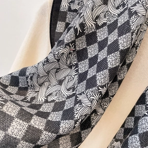 Detail of checkered silk scarf with wavy patterns on a white knitted sweater