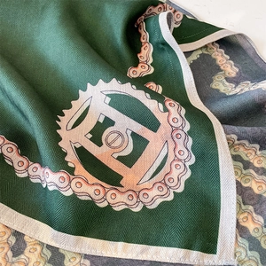 Green silk square scarf with orange chain patterns and herringbone texture detail