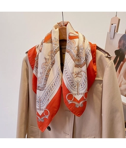 Detail of silk feel scarf with equestrian chain print draped on a beige trench coat