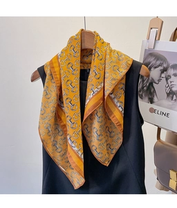 Detail of yellow silk scarf with metal horsebit chain print on a wooden hanger