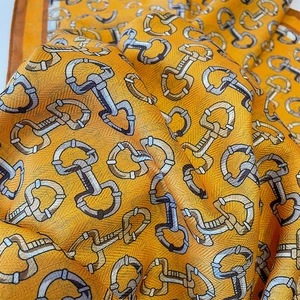 Detail of orange cotton-linen scarf featuring golden horsebit pattern and twill texture
