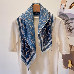 Blue geometric silk scarf with horsebit print on a white knit sweater and wooden hanger