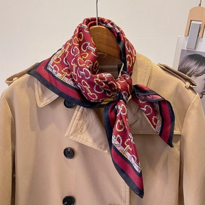Detail of red and black geometric silk scarf with gold chain print on a khaki coat