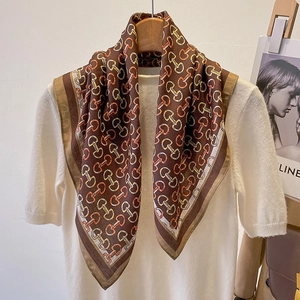 Detail of a brown silk scarf with chain print draped over a white knitted sweater