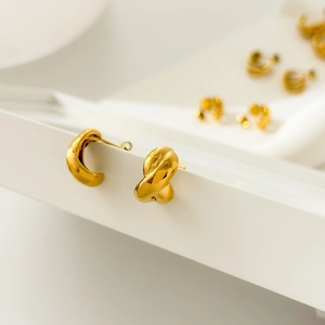Detailed macro view of 18K gold plated twisted croissant earrings on a white stand