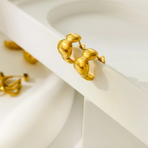 Close-up of golden curved croissant-style stud earrings on white geometric stands