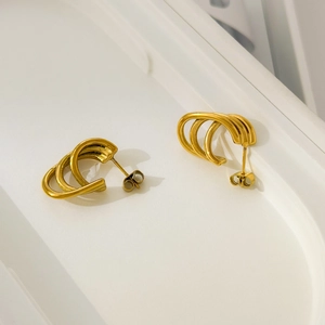 Detail view of gold-plated triple-layered curved stud earrings with a 3D arc design