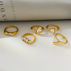 Detailed close-up of five 18K gold plated rings with various zircon stone shapes on white surface