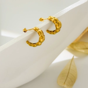 Detail of gold C-shaped quilted hoop earrings with polished croissant texture on white stand