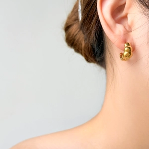 Minimalist golden croissant dome hoop earring with textured ribbing on female model