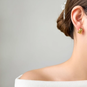 Close-up of a model wearing the golden twisted dome earrings with polished finish
